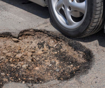 Close-up of a car tire next to a large pothole on an asphalt road